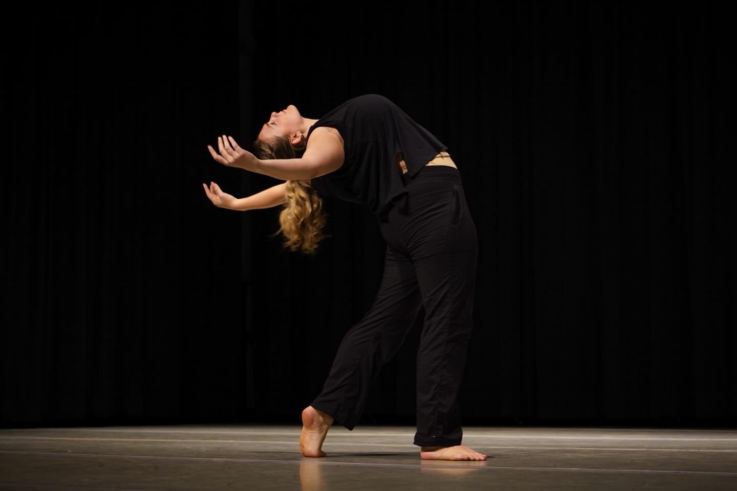 Solo contemporary dancer arches backward with arms open on a dimly lit stage.