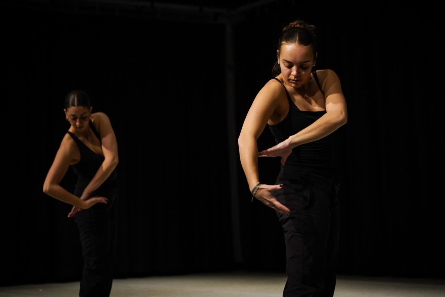 Contemporary dancer performs precise hand and arm gestures in a darkened stage setting.